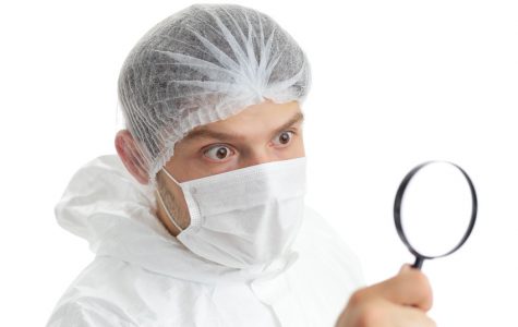 Medical staff member with a magnifying glass in front of his eye; isolated on white background